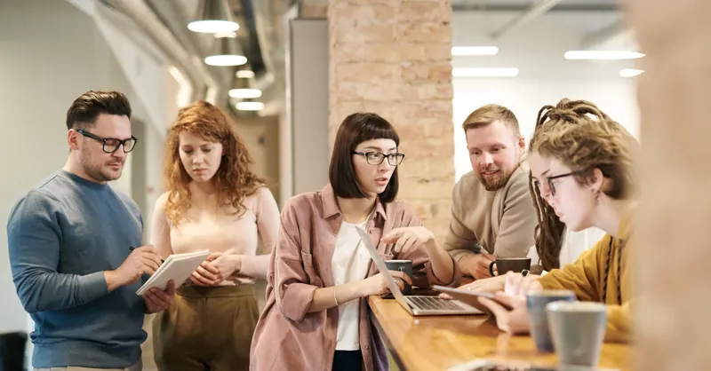 A diverse group of coworkers in a modern office engaged in teamwork using technology.
