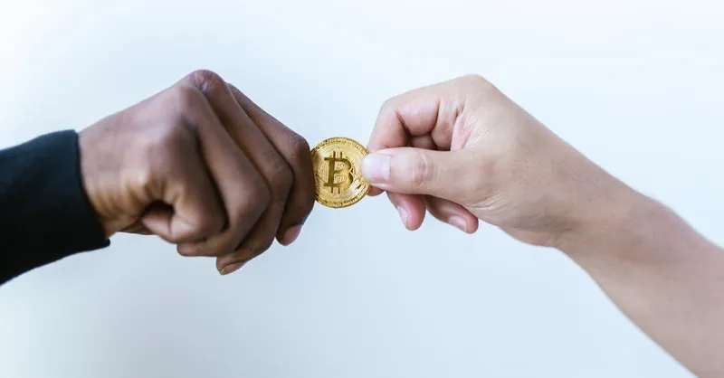 Two hands exchanging a Bitcoin coin, symbolizing cryptocurrency transactions.