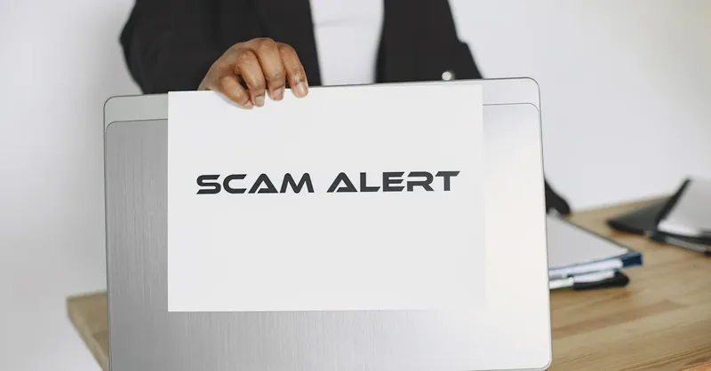 Business person holding a scam alert sign over a laptop, warning against online fraud.