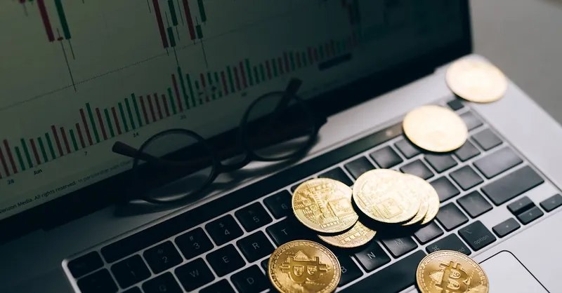 Golden Bitcoins on a laptop keyboard with a stock market chart on the screen, symbolizing cryptocurrency trading.