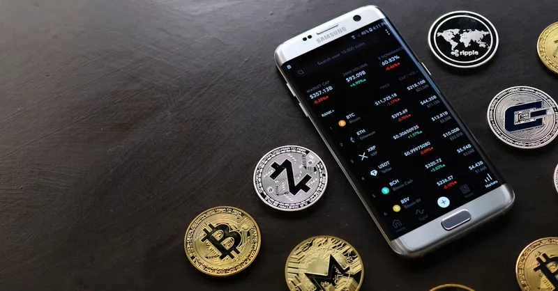 A collection of cryptocurrency coins and a smartphone displaying a digital trading platform.