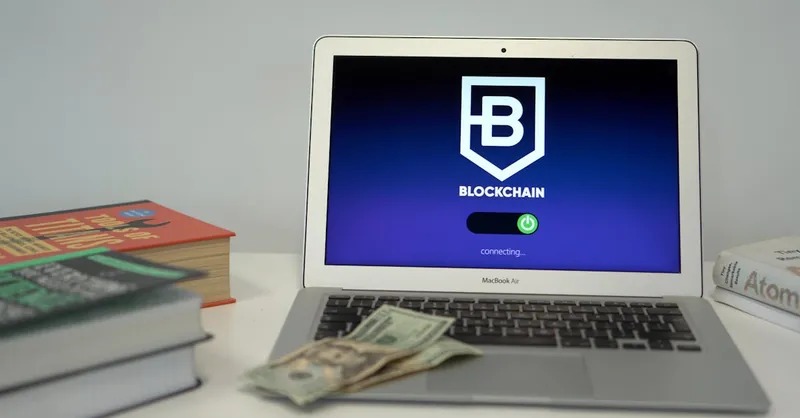 Laptop showing blockchain connection screen on desk with books and US dollars.
