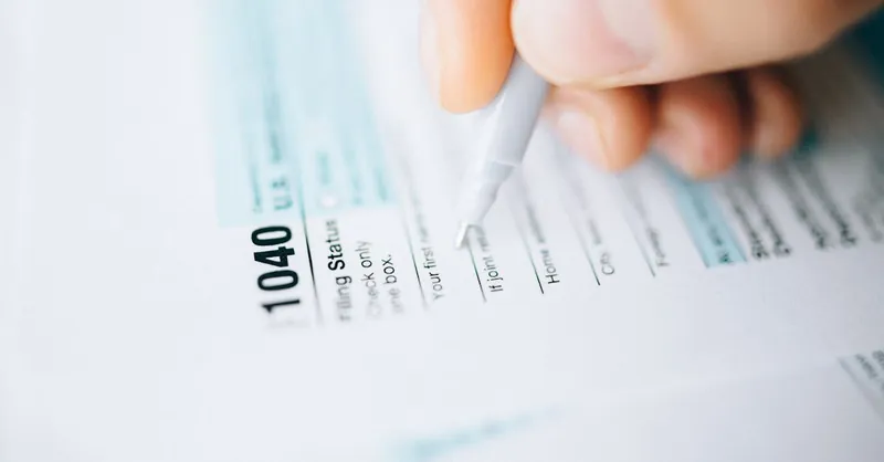 Close-up of a hand using a pen to fill out a tax form 1040, focusing on details.