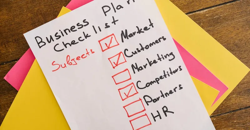 A handwritten business plan checklist on a table with colorful papers indicating important topics for startups.