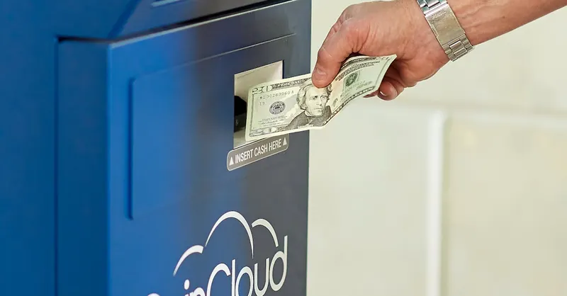 Hand inserting cash into a CoinCloud ATM, illustrating cryptocurrency exchange process.