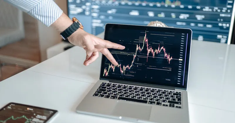 A person pointing at a laptop displaying a cryptocurrency market chart, indicating data analysis.